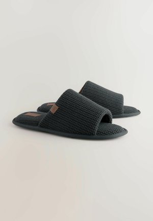 Papuci gri cu degetul liber, textura cu un model țesut și talpă plată. Au o etichetă de accent maro pe o parte. Design minimalist.