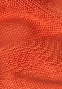 Tessuto a maglia testurizzato di color arancione brillante, caratterizzato da un motivo geometrico con sezioni in rilievo. Materiale morbido con dettagli di cucitura visibili.