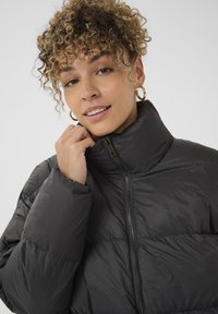 Giubbotto piumino nero con colletto alto, dotato di zip frontale, texture trapuntata e polsini elasticizzati. Materiale morbido e leggero.