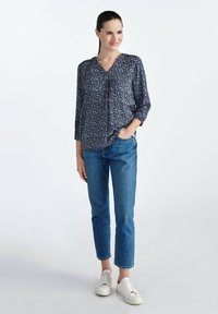 Granatowa bluzka w kwiatowy wzór, dekolt w serek i rękawy o długości trzech kwartałów; zestawiona z jasnoniebieskimi dżinsami i białymi trampkami.