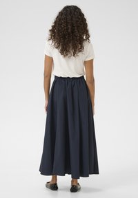 Gonna lunga blu navy con elastico in vita. Tessuto liscio e fluido che scende fino alle caviglie, abbinata a una maglietta di colore chiaro e scarpe nere.