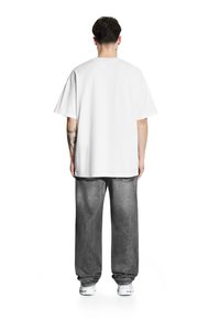 Biała bawełniana koszulka o luźnym kroju, z krótkim rękawem i okrągłym dekoltem. Połączona z luźnymi, wyblakłymi szarymi dżinsami i trampkami.