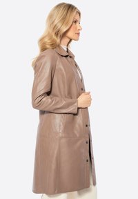 Bruine leren jas met een kraag, knoopsluiting en zijzakken. Gladde textuur, knielange ontwerp en aansluitende silhoeet.