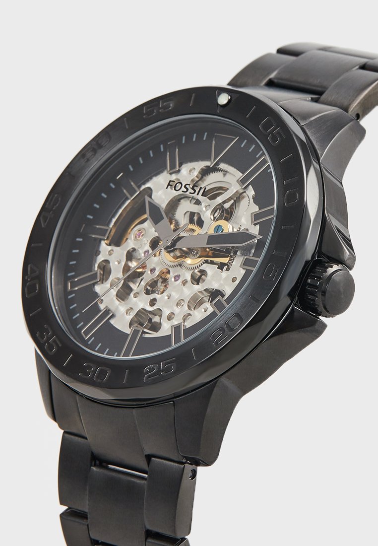 Orologio scheletro Fossil con cinturino in acciaio inossidabile nero, cassa rotonda, faccia trasparente e dettagli dorati visibili attraverso il design scheletrico.