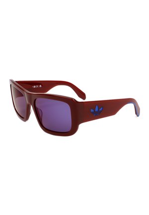 Occhiali da sole rettangolari con lenti viola, montatura spessa rossa e logo Adidas blu sulla stanghetta.