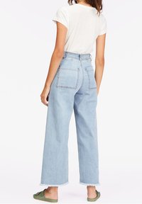 Jeans de pierna ancha de tiro alto en un tono azul claro con un dobladillo sin terminar, que cuentan con dos bolsillos traseros y una textura de denim suave. Combinados con una camiseta blanca.