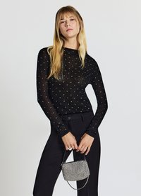 Top nero a maniche lunghe con texture a coste e pois bianchi, abbinato a pantaloni neri e una piccola borsa argento con borchie.