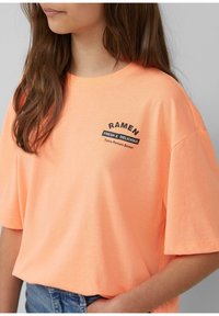 Heldere oranje katoenen t-shirt met korte mouwen, voorzien van zwarte tekst: "RAMEN FRESH & DELICIOUS" en "Tokio Ramen Street" aan de voorkant.