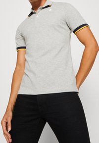 Polo grigia con maniche corte, caratterizzata da accenti a strisce blu navy e gialle sul colletto e sulle maniche. Tessuto morbido e liscio.