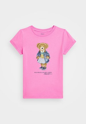 T-shirt rose à manches courtes avec un ours en peluche portant une veste, une jupe et des baskets imprimé au centre.