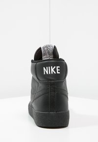 Schwarze High-Top-Sneaker aus strukturiertem Leder, mit gepolstertem Kragen und weißem Logo hinten. Gummisohle mit strukturiertem Muster.