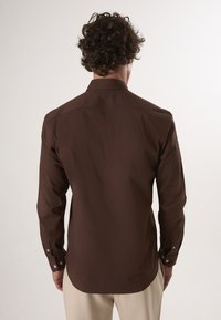 Camicia a maniche lunghe marrone scuro realizzata in tessuto morbido, con colletto classico e polsini abbottonati, vista dal retro.