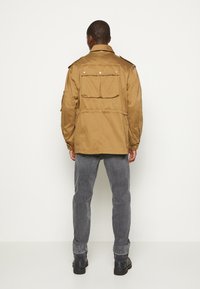 Kurtka wojskowa khaki z dwiema tylnymi kieszeniami, pagonami na ramionach i ściągaczem w pasie. Połączona z szarymi dżinsami i czarnymi butami.