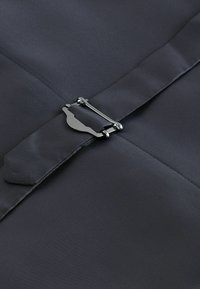 Grijze stof met een gladde textuur, voorzien van een metalen gesp en riemdetails. De stof heeft een subtiele glans en is netjes gevouwen.