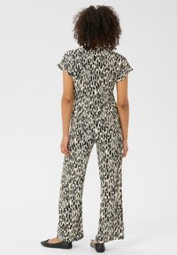 Sort og creme dyreprint outfit med en kortærmet top og brede bukser. Stoffet har en glat tekstur med et flydende design.