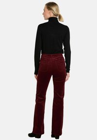 Suéter negro de cuello alto y pantalones de pana burdeos acampanados. Los pantalones cuentan con bolsillos traseros y un acabado texturizado. Modelo mostrado de espaldas.
