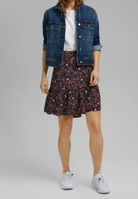 Jeansjack over een wit T-shirt, gecombineerd met een donkere bloemenrok met een gerimpelde zoom en witte sneakers.