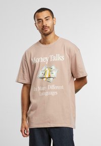 Tricou bej, cu mânecă scurtă, lejer, cu imprimeu grafic cu bani și textul "Banii vorbesc în multe limbi diferite." Material din bumbac.