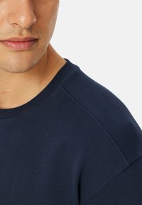 Granatowy sweter z okrągłym dekoltem, żebrowanym kołnierzem oraz miękkim materiałem o schludnym wykończeniu. Widoczne detale przeszycia na ramionach.