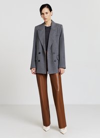 Grauer zweireihiger Blazer mit tailliertem Schnitt, kombiniert mit braunen, aus Kunstleder gefertigten Straight-Leg-Hosen und weißen spitzen Schuhen.