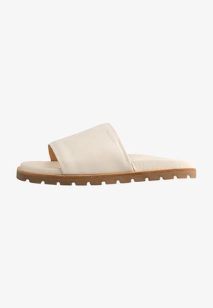 Slide sandal made of cream leather with a wide strap, textured upper, and a flat rubber sole featuring a lug pattern for traction.