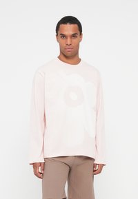 Camicia a maniche lunghe rosa chiaro con una grande stampa floreale bianca. Materiale morbido e vestibilità comoda, con collo tondo e orlo dritto.