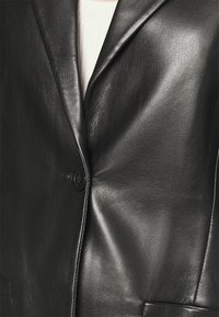 Czarna skórzana marynarka o gładkim wykończeniu, z pojedynczym zapięciem na guzik i klapami z wycięciem. Posiada dwie boczne kieszenie oraz dopasowany krój.