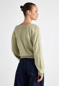 Lichtgroene sweater met een wijde halslijn, verlaagde schouders en lange mouwen. Draagt met donkerblauwe high-waisted jeans, die een eenvoudig ontwerp tonen.