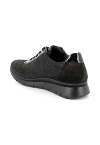 Sneaker nera a profilo basso con tessuto testurizzato, chiusura a lacci frontale, dettaglio lucido sul tallone e suola spessa e imbottita inclinata di lato.