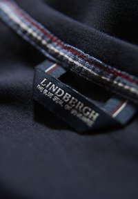 Granatowy materiał z widoczną metką z napisem "LINDBERGH" oraz "NIEBIESKIE SEAL SZWECJI". Szycie ma czerwono-białe akcenty.