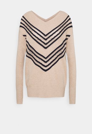 Pull beige en tricot avec manches longues, col en V et rayures chevrons noires avec des détails en maille ajourée à l'avant et sur les manches.
