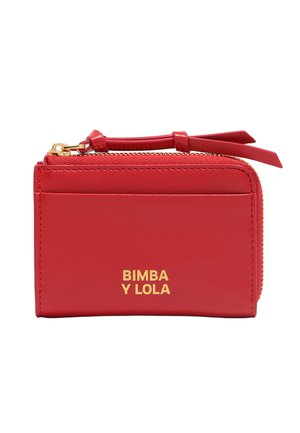 Cartera de piel roja con cremallera dorada y logo. Presenta una forma rectangular compacta, textura suave y una pequeña correa para la muñeca que facilita su transporte.