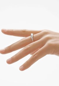 Anillo de plata con un diseño en forma de lágrima, textura suave, ajustado en un dedo. Se puede ver el tono de piel, lo que enfatiza el brillo del anillo.