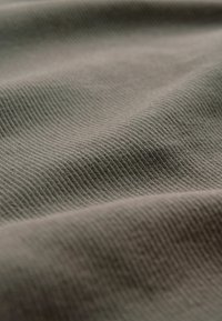 Mutezovaná zelená látka s jemnou, ryhovanou textúrou. Povrch vykazuje jemné variácie odtieňa a hladký, plynulý vzhľad.