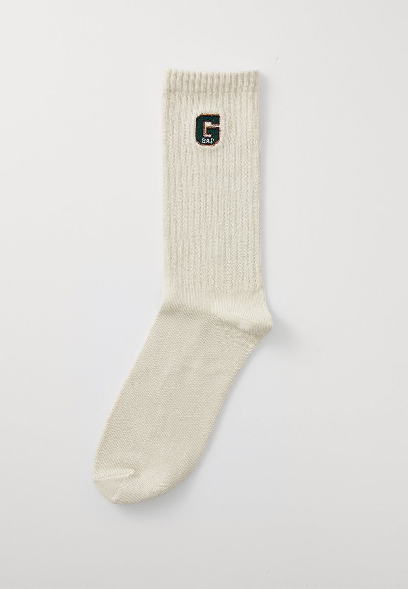 Kniestrümpfe in cremefarben mit Rippmuster und einem kontrastierenden, gestickten "G"-Emblem in Grün und Schwarz auf der Oberseite.