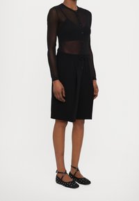 Černý průsvitný top s dlouhými rukávy a knoflíky, doplněný černými šortkami ke kolenům. Obuv je černá s puntíky a má kotníkový popruh.