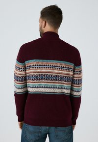 Bordeaux gebreide trui met een patroon op de schouder in blauw, crème en bruin, met een hoge kraag en geribde manchetten en zoom.