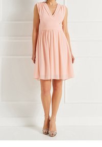 Růžové bezrukávové šaty s výstřihem do V a nařaseným pasem, dosahujícími do poloviny stehna. Hladká tkanina s splývavou sukní. Jednoduchý design.