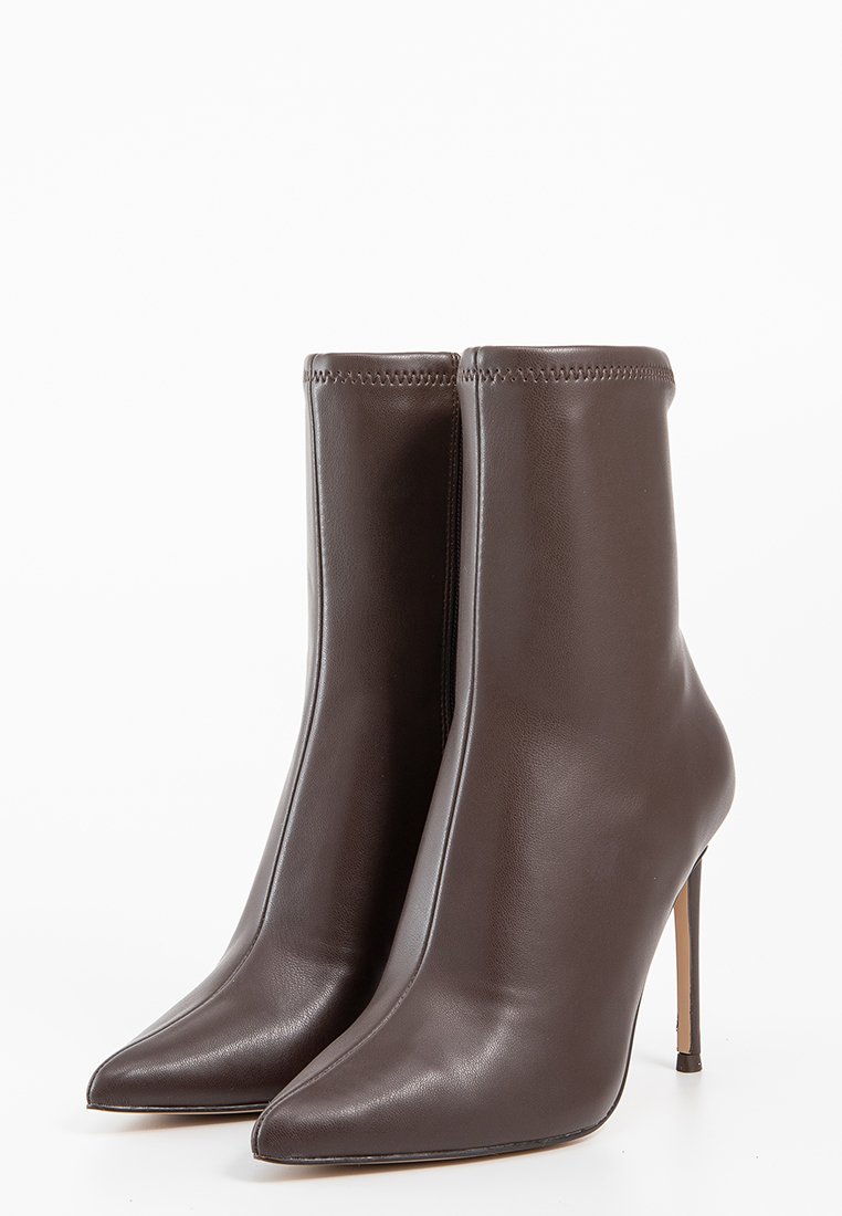 Bottes en cuir marron à cheville avec un bout pointu, un talon stiletto haut, une texture lisse et des détails cousus le long du bord supérieur.