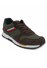 Sneaker verde oliva con accenti in suede marrone, suola intermedia bianca, suola nera e strisce rosse e gialle sui lati. Design della punta arrotondata.