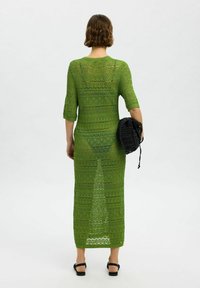 Vestido de ganchillo verde hasta la rodilla con un patrón geométrico, mangas tres cuartos y un corte holgado. Se lleva con una bolsa negra con cuerda.