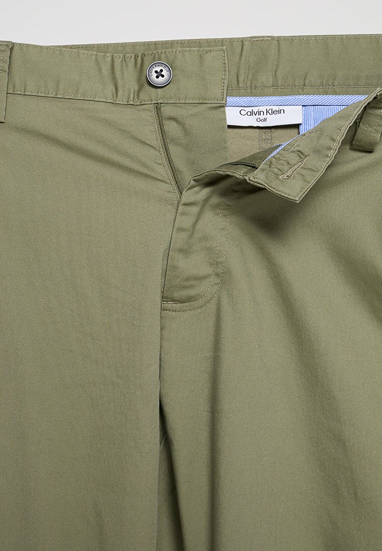 Olijfgroene broek met een knoopsluiting, met een label dat "Calvin Klein Golf" zegt en van een gestructureerde katoenstof is.