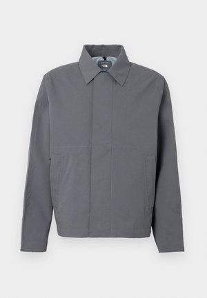 Graue, leichte Jacke mit Kragen, Frontreißverschluss und zwei Seitentaschen. Glatte Textur und minimalistisches Design mit dezenten Steppnähten.