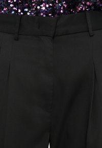 Čierne módne nohavice so štruktúrovanou textúrou, rovný strih, predné záhyby a púzdra na opasok, doplnené trblietavým topom.