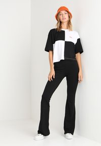 T-shirt cropped bicolore noir et blanc à manches courtes, associé à un pantalon évasé noir et des sneakers blanches. Chapeau seau orange inclus.