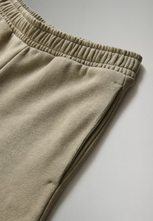 Pantaloni della tuta beige con cintura elastica, realizzati in materiale morbido. Presentano una texture liscia e tasche laterali a fessura.
