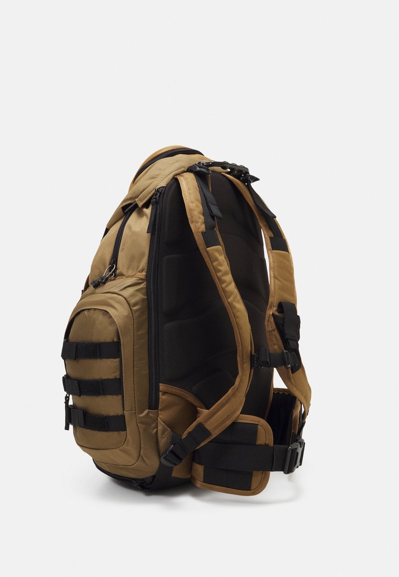 Zaino in stile tattico in tonalità sabbia e nero. Presenta spallacci imbottiti, numerosi scomparti esterni con zip e una superficie texturizzata.