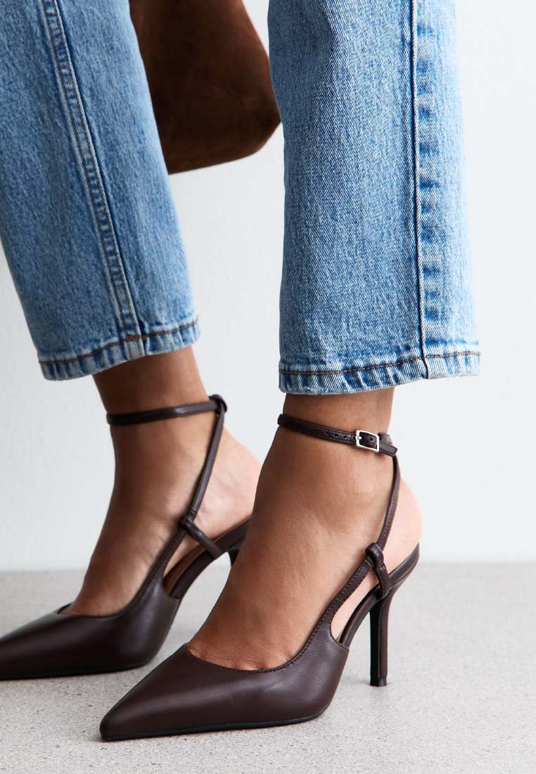 Bruna läderhögklackade skor med spetsig tå, ankelrem och öppen häl. Bärs med blå cropped jeans. Slät textur.