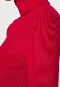 Red ribbed turtleneck sweater featuring a close-fitting design, textured fabric, and a high collar.
