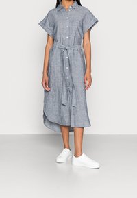 Robe chemise rayée bleue et blanche avec des manches courtes, une ceinture à la taille et une longueur midi, associée à des sneakers blanches.